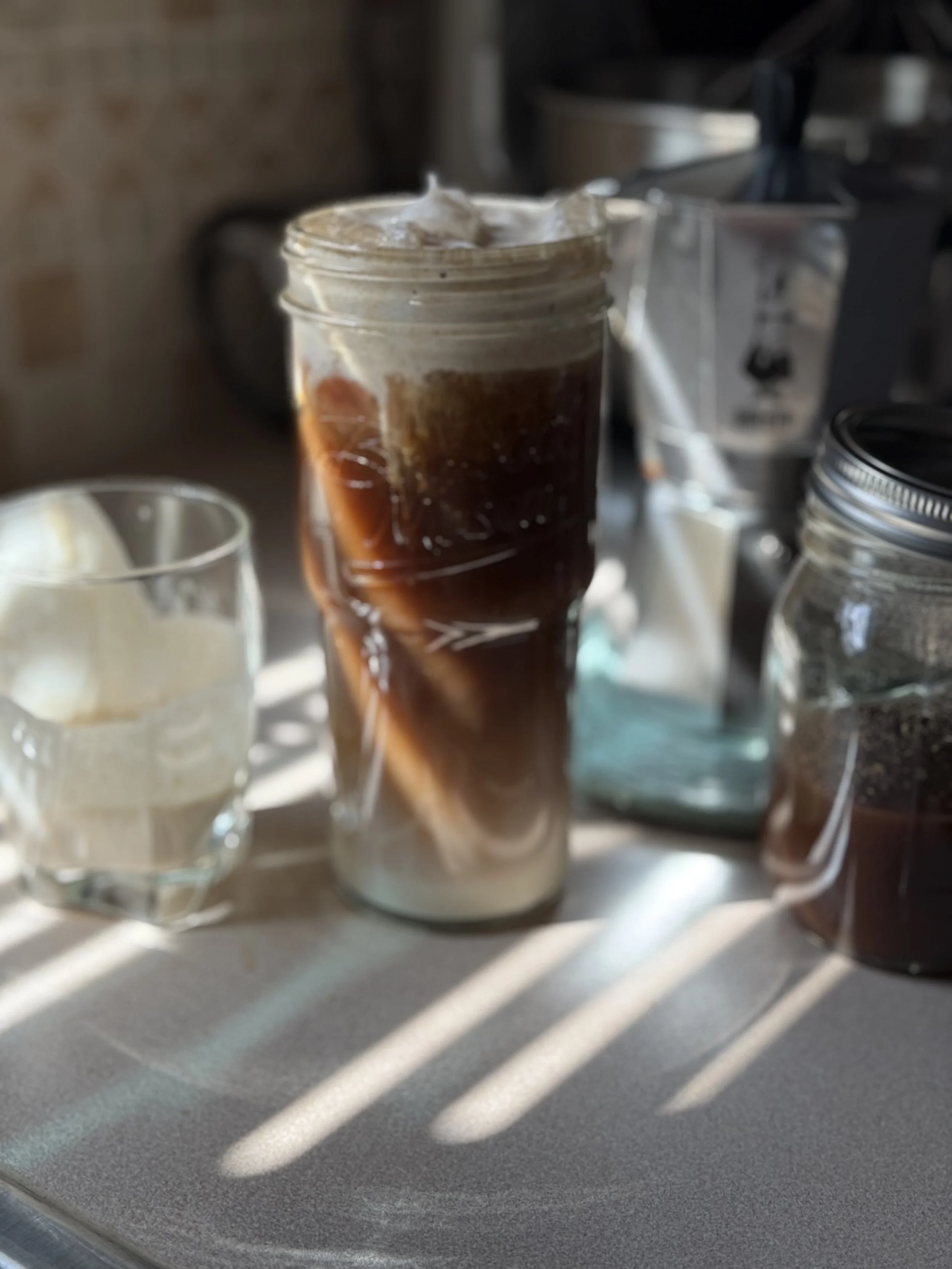A glass of iced coffee on a kitchen countertop with sunlight and shadow patterns.