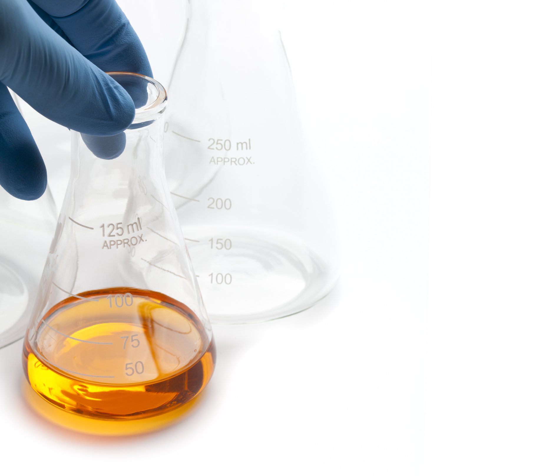 Hand in a blue glove holding a small glass beaker with orange liquid on a white laboratory surface, with two empty glass beakers in the background.
