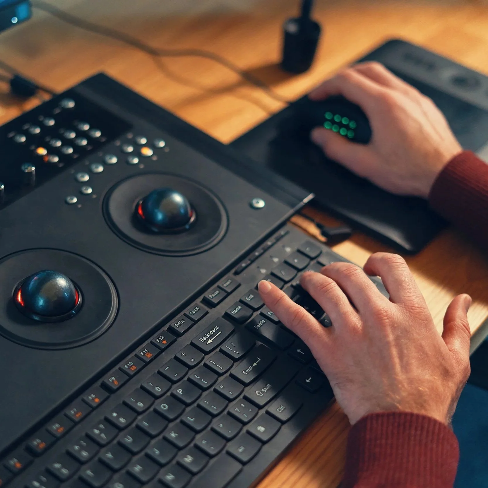 A person using a DJ controller with a keyboard on a wooden desk.