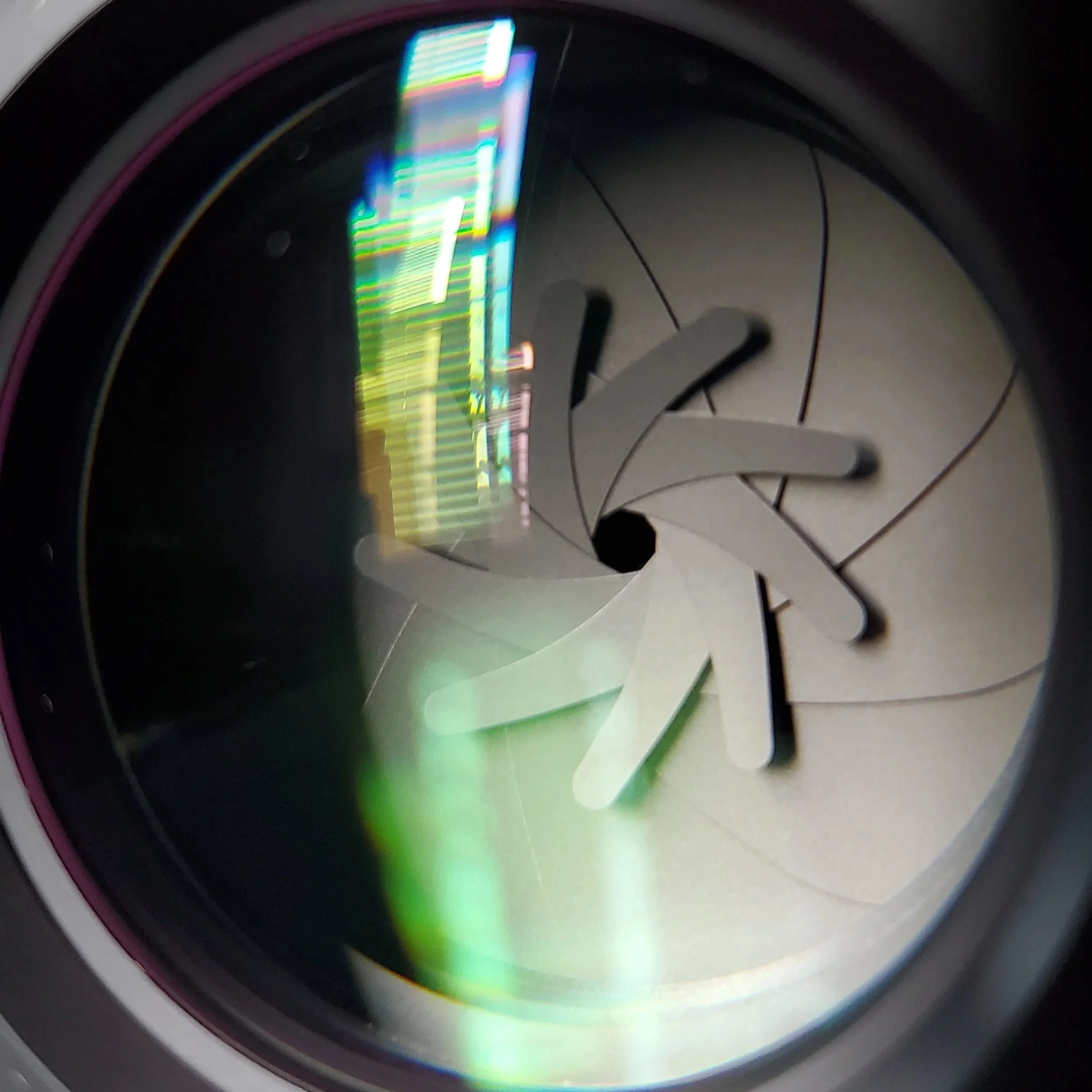 Inside view of a camera or printer lens showing the aperture blades and a colorful reflection.