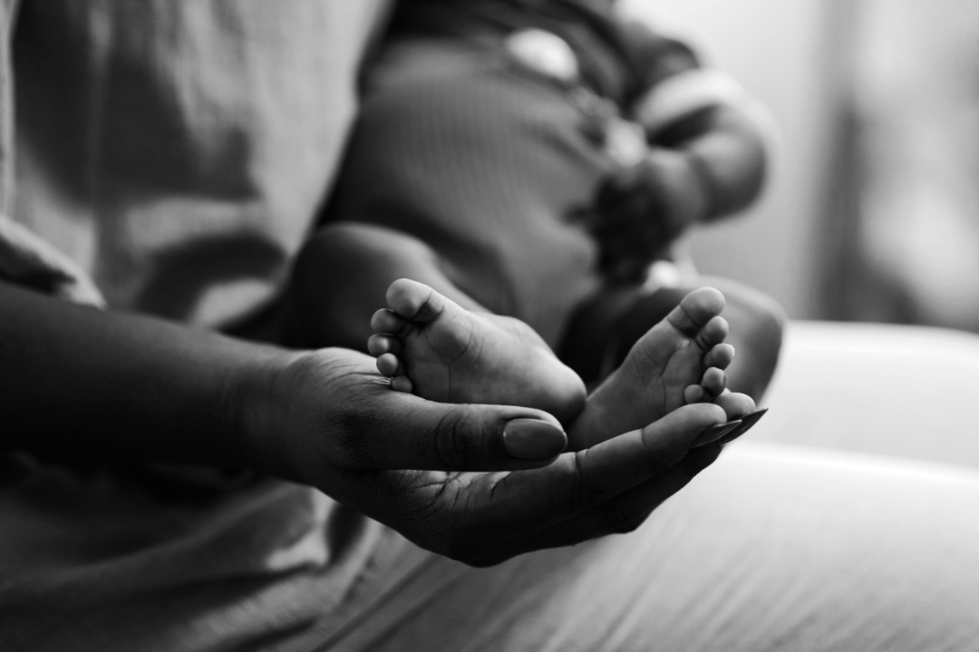 Close-up of an adult's hand holding a baby's feet in black and white.