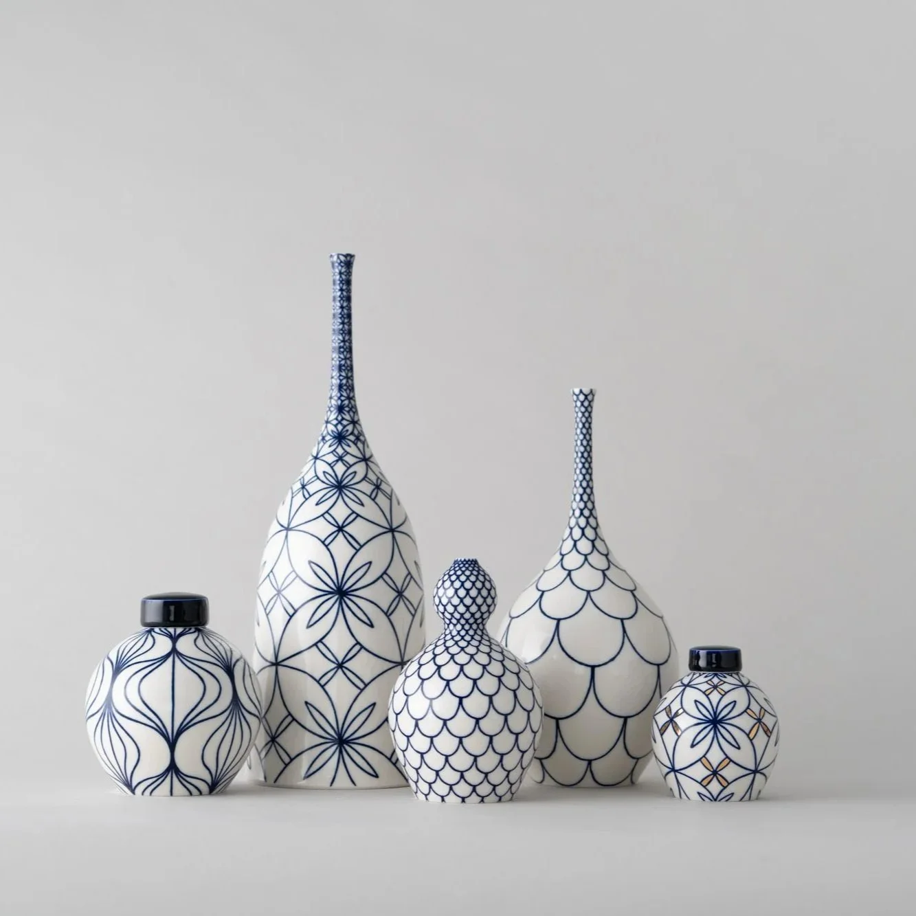 Set of five white ceramic vases with blue geometric patterns on a light gray background.