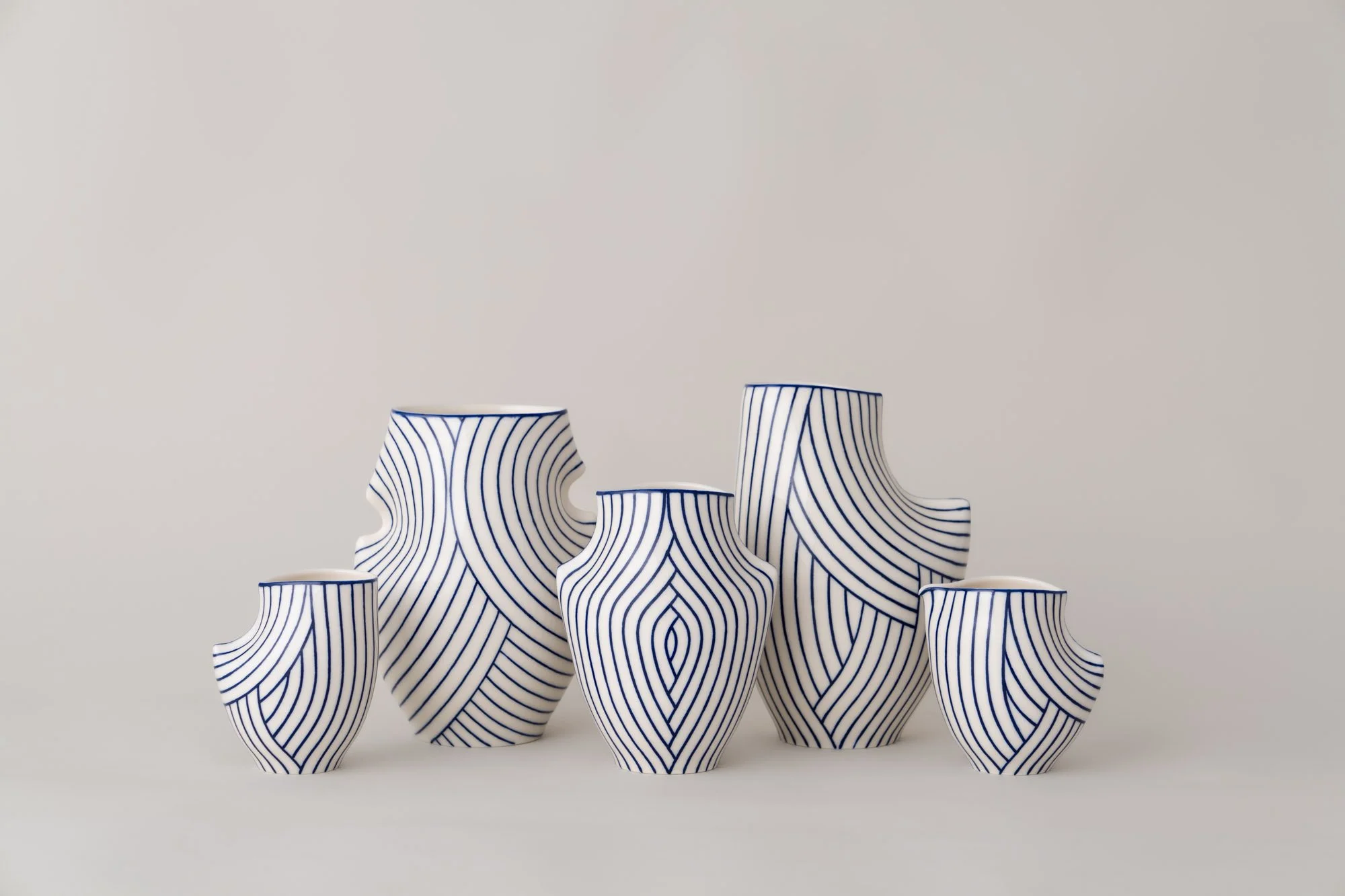 Set of six vases with white and blue striped patterns, arranged on a plain surface against a plain background.