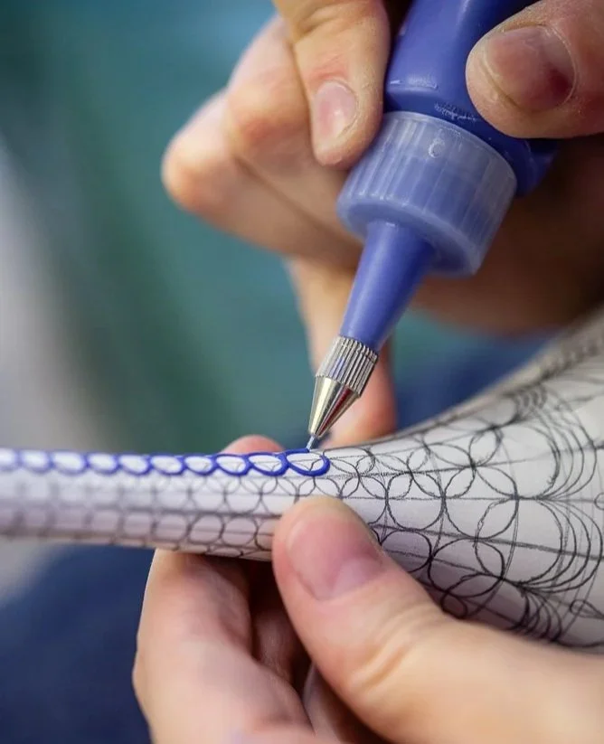 Close-up of a person using a blue marking pen to draw circular patterns on a cylindrical object.