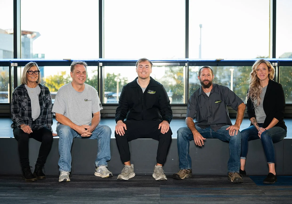 Trade Show and Retail I and D team sitting on a bench in a bright space with large windows and outdoor trees in view.