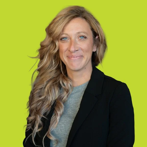 Woman smiling, wearing a gray shirt and black blazer, against a lime green background.