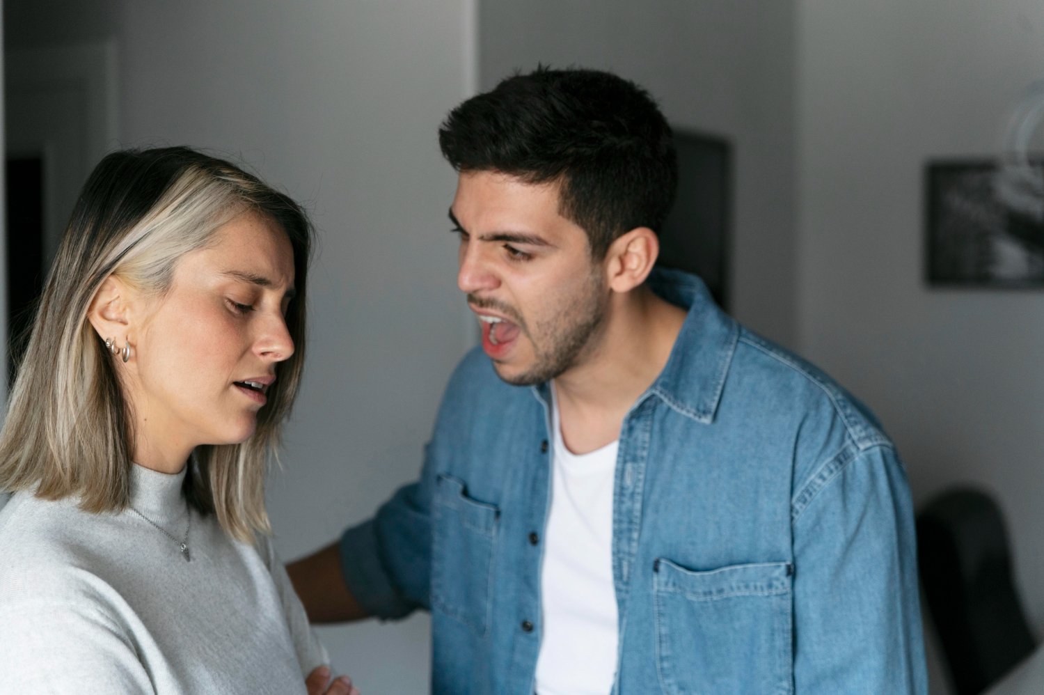 A young man appears to be yelling at or scolding a young woman with closed eyes, in an indoor setting.