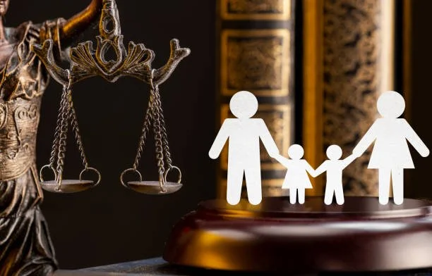 Paper cutouts of a family holding hands, with a scale of justice and legal books in the background.