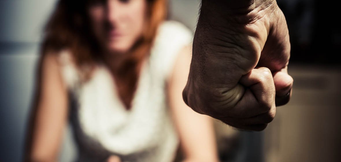 Close-up of a clenched fist with a woman in the blurred background showing frustration or anger.