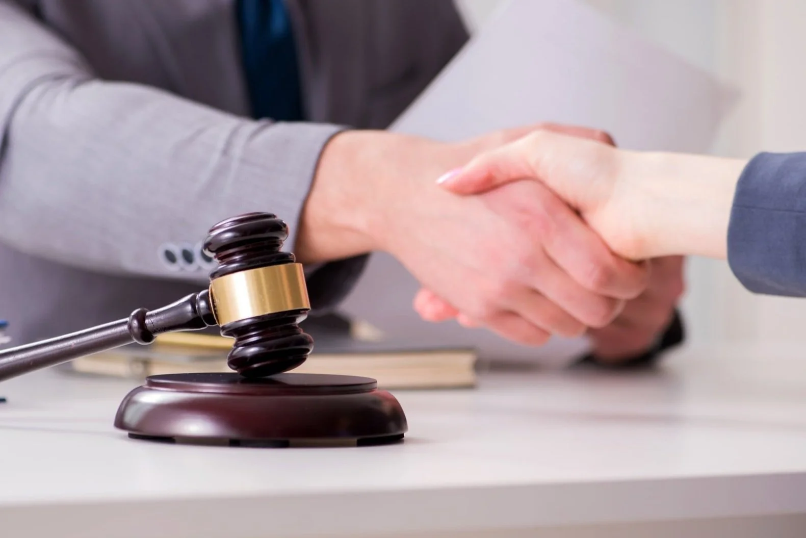 A gavel resting on a table near a handshake between two people, indicating a legal or court-related setting.