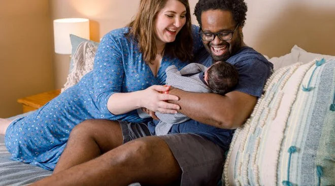 A happy couple with a newborn baby on a bed in a cozy bedroom.