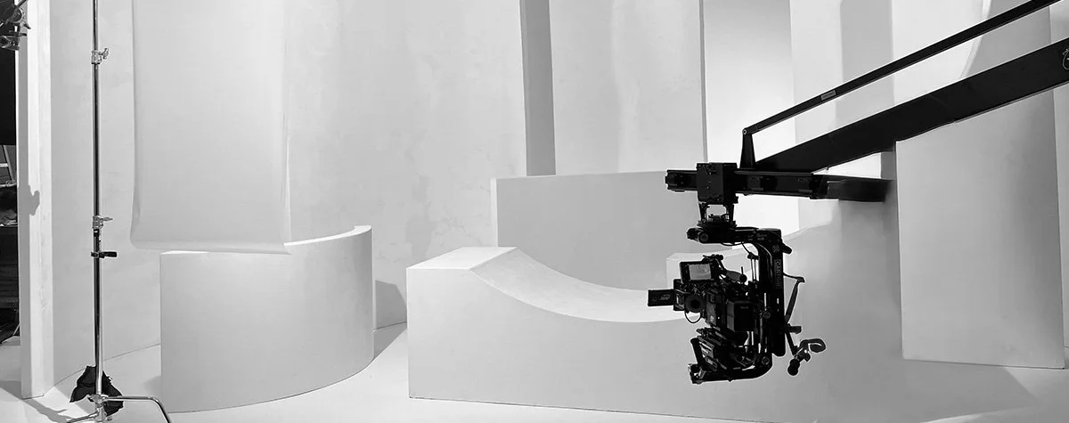 Black camera crane setup in a minimalist white studio with curved and rectangular platforms.
