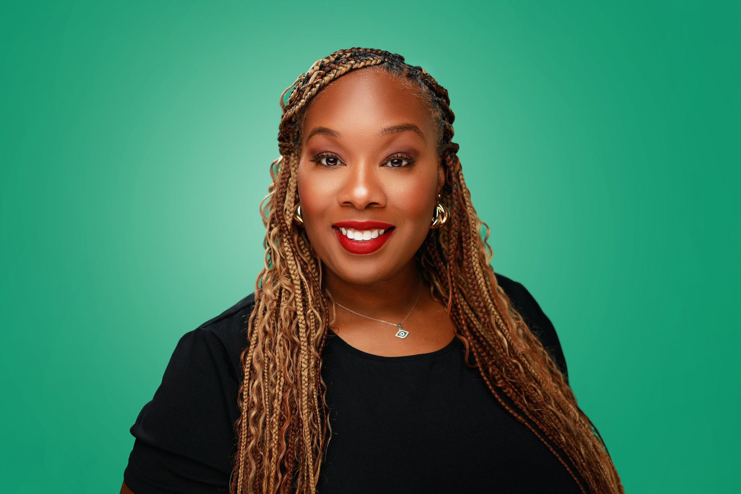 A woman with long braided hair smiling against a green background.