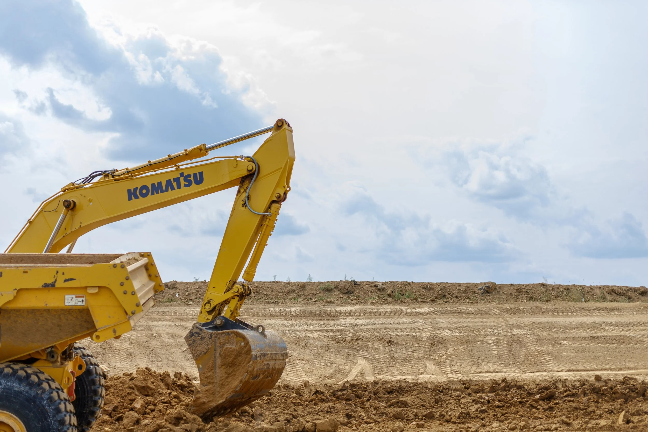 Yellow Komatsu excavator on a construction site with dirt and a cloudy sky.