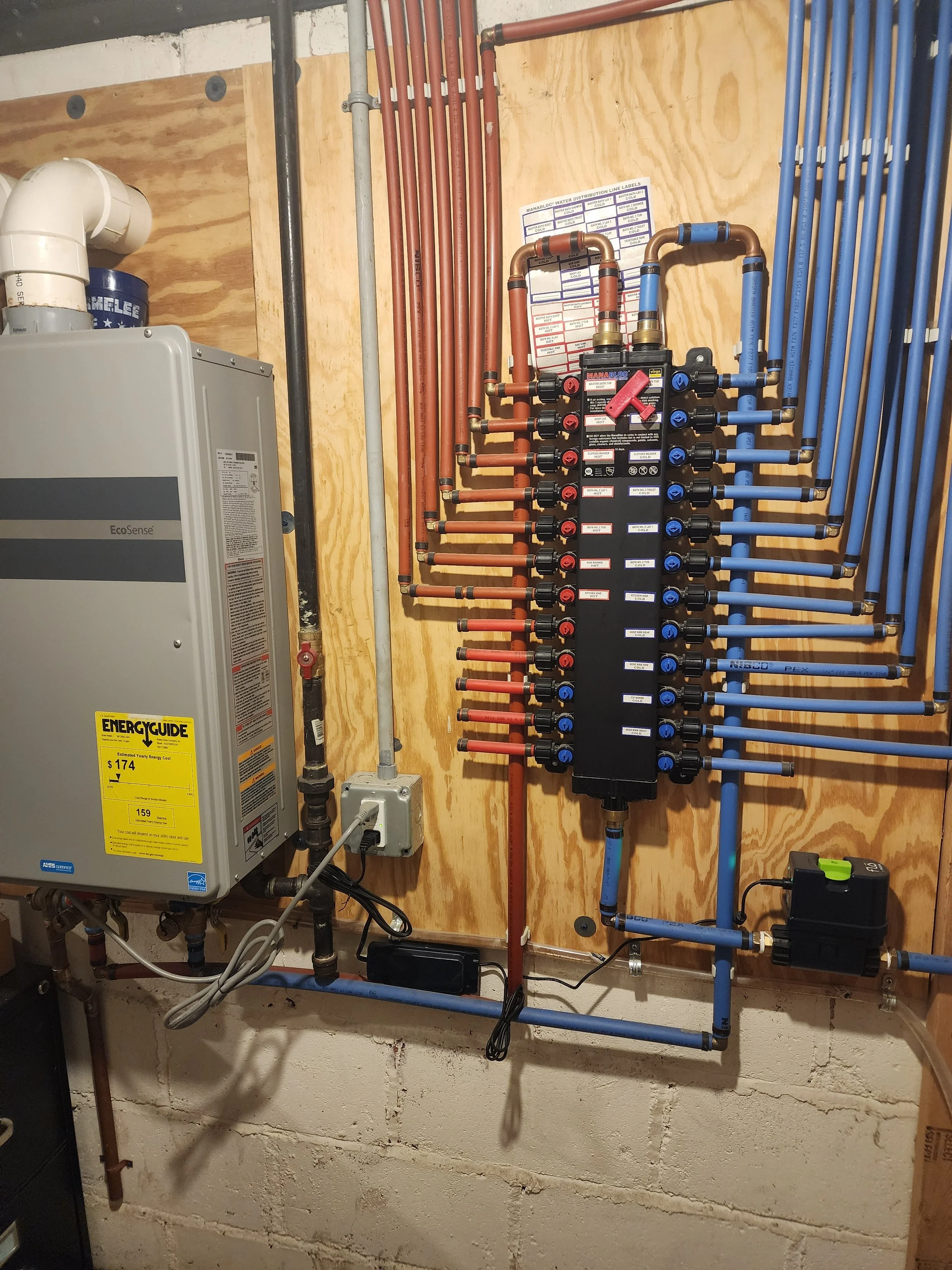 A plumbing manifold with multiple red and blue PEX pipes connected, mounted on a plywood wall, with a boiler and various pipes nearby.  Annual home maintenance services include flushing your water heater, blowing out HVAC units, and changing filters