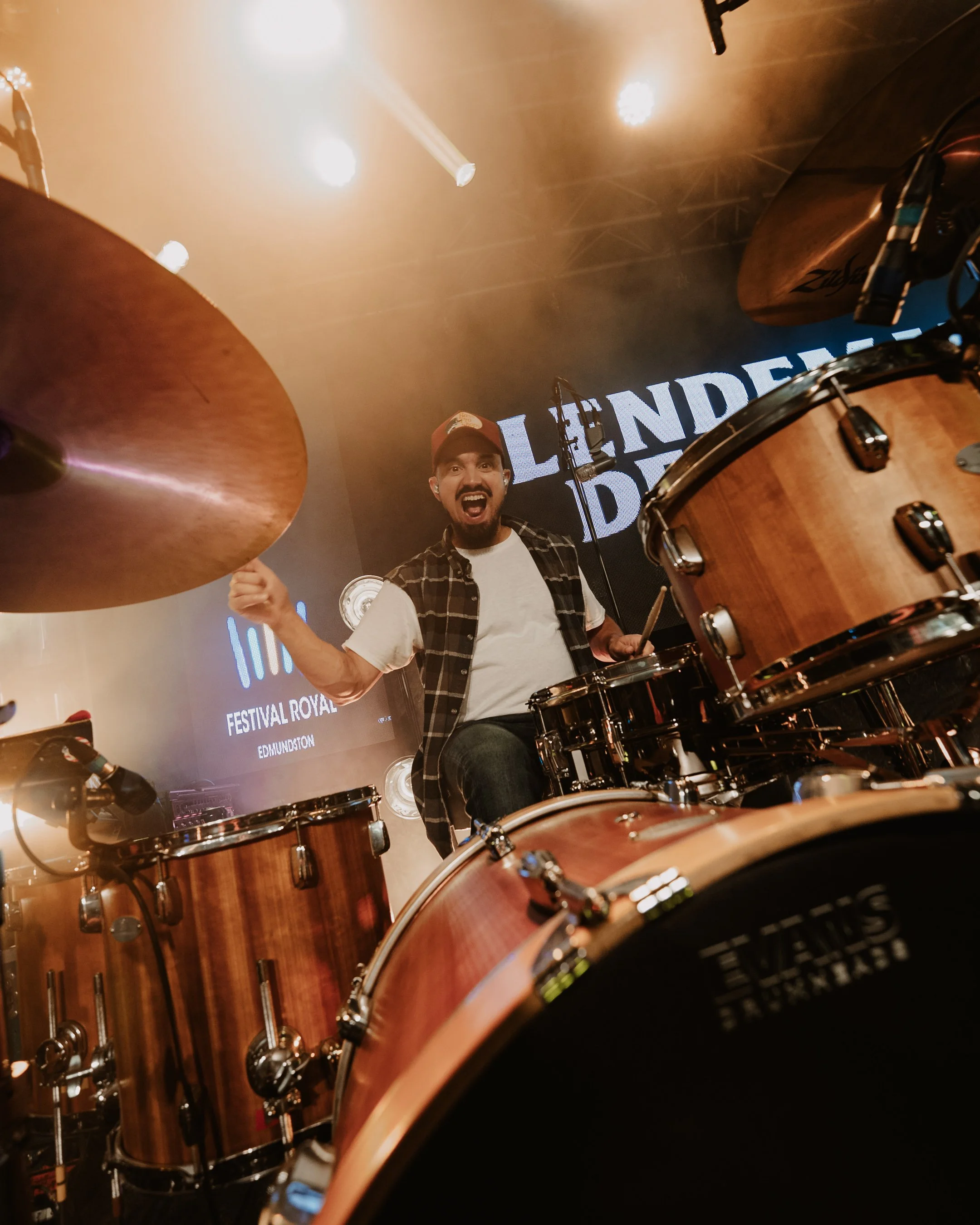 Un homme jouant de la batterie sur scène avec des lumières de spectacle en arrière-plan.