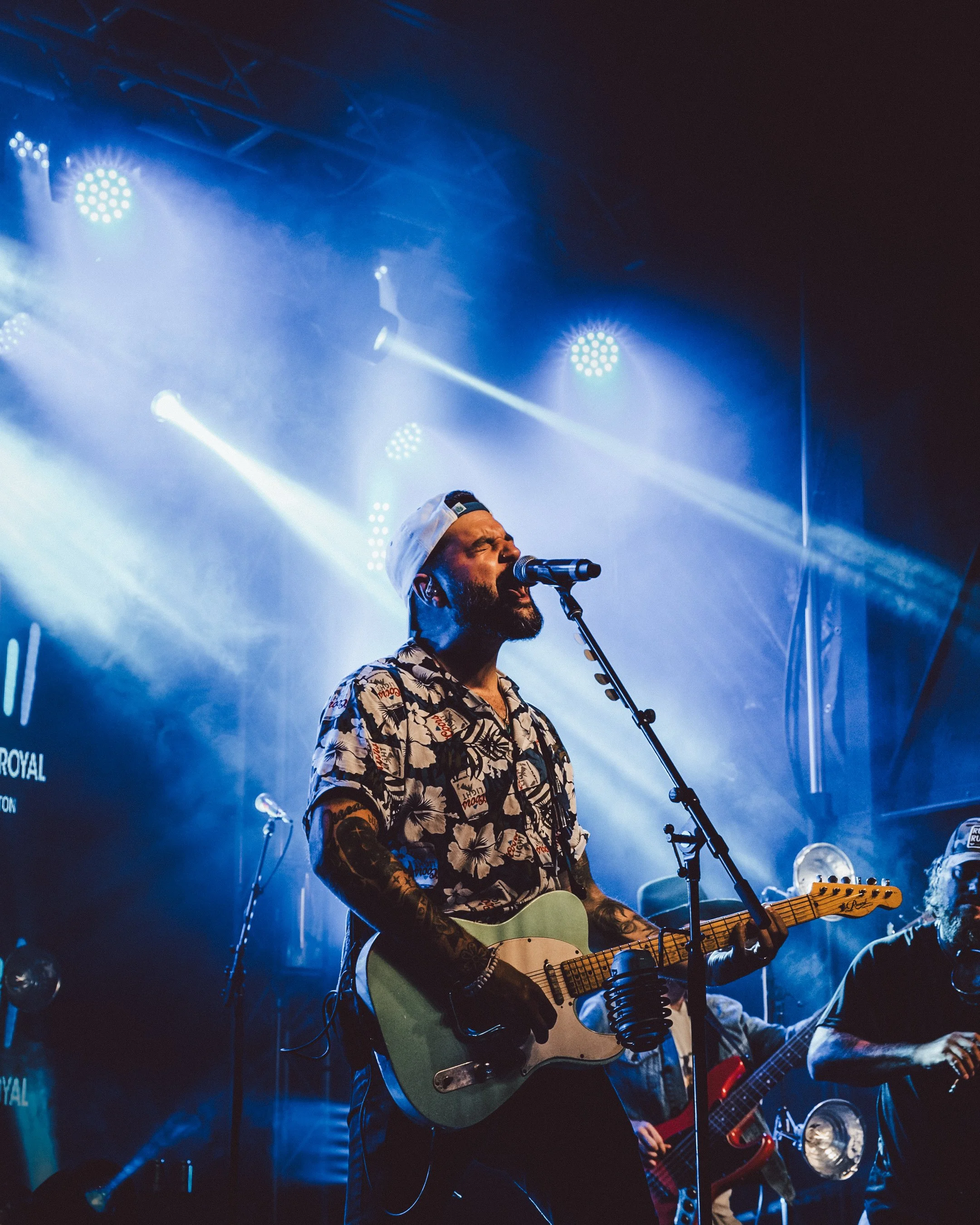 Un homme joue de la guitare et chante dans un concert, sous des lumières vives et colorées.