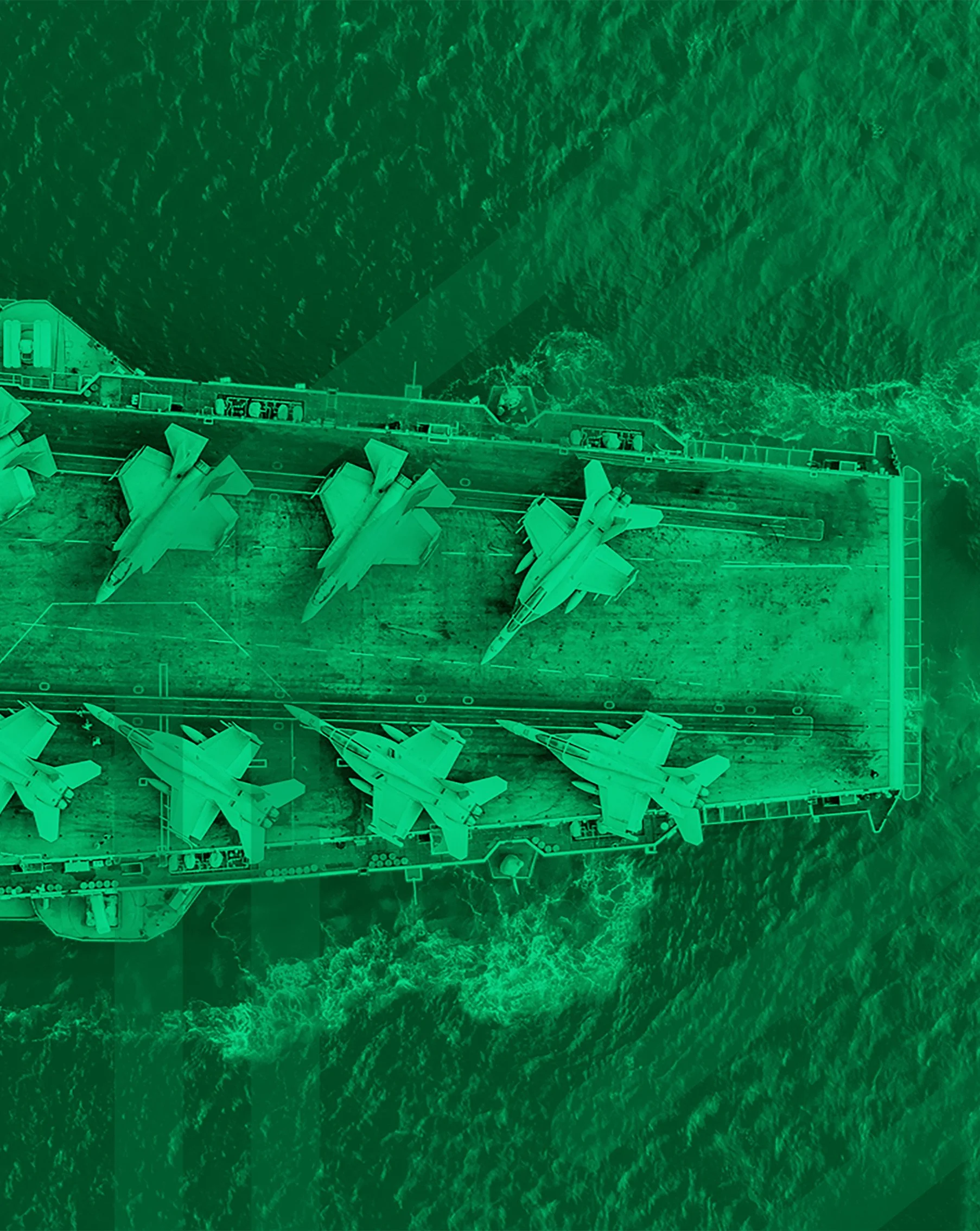 Aerial view of an aircraft carrier at sea, with several fighter jets parked on the deck, surrounded by ocean waves.