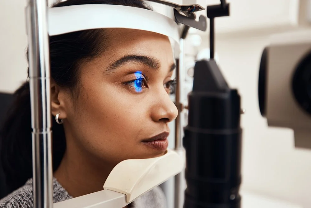 A woman undergoing an eye examination using a slit lamp with a blue light reflected in her eye.