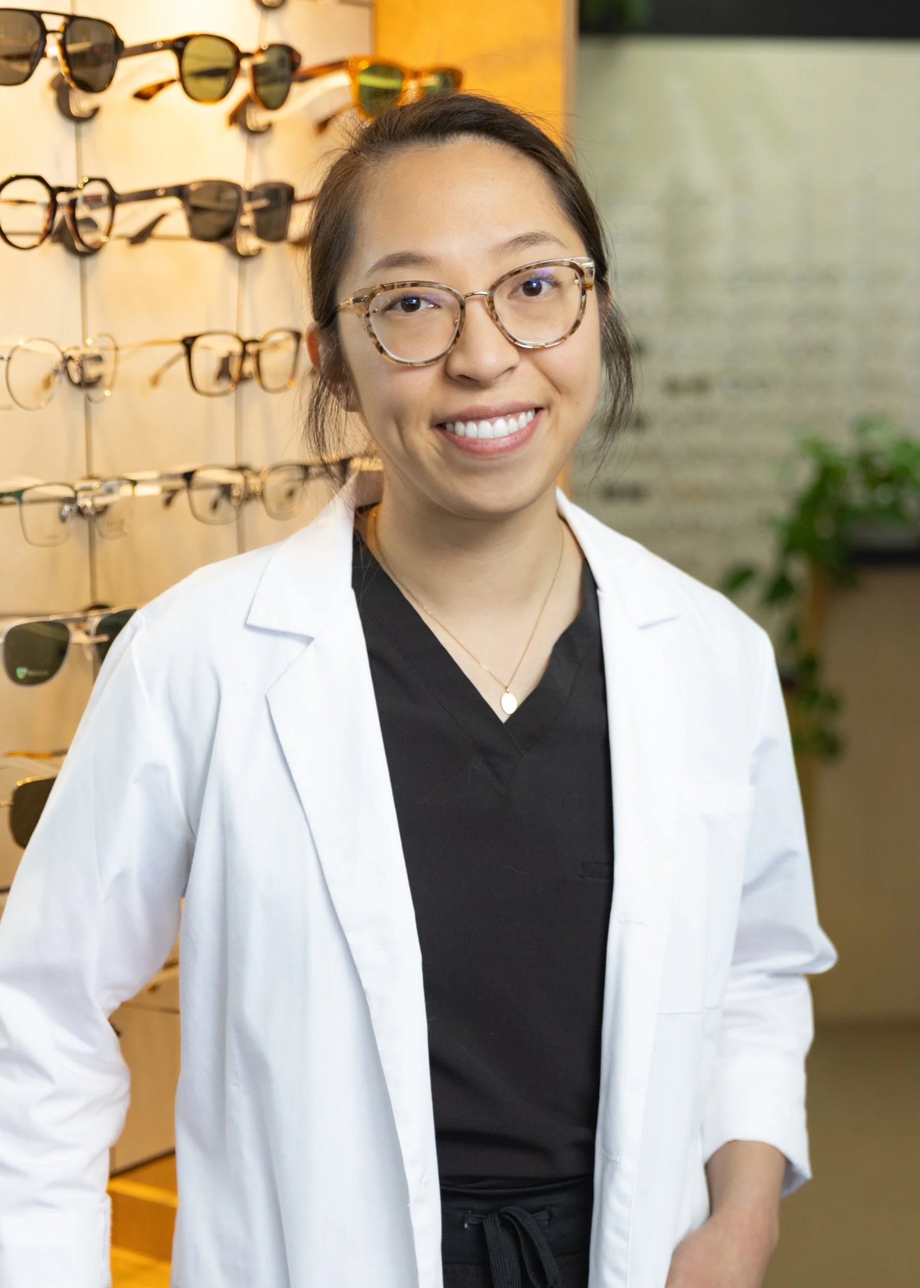 A woman wearing glasses and a white lab coat standing in front of display of sunglasses.