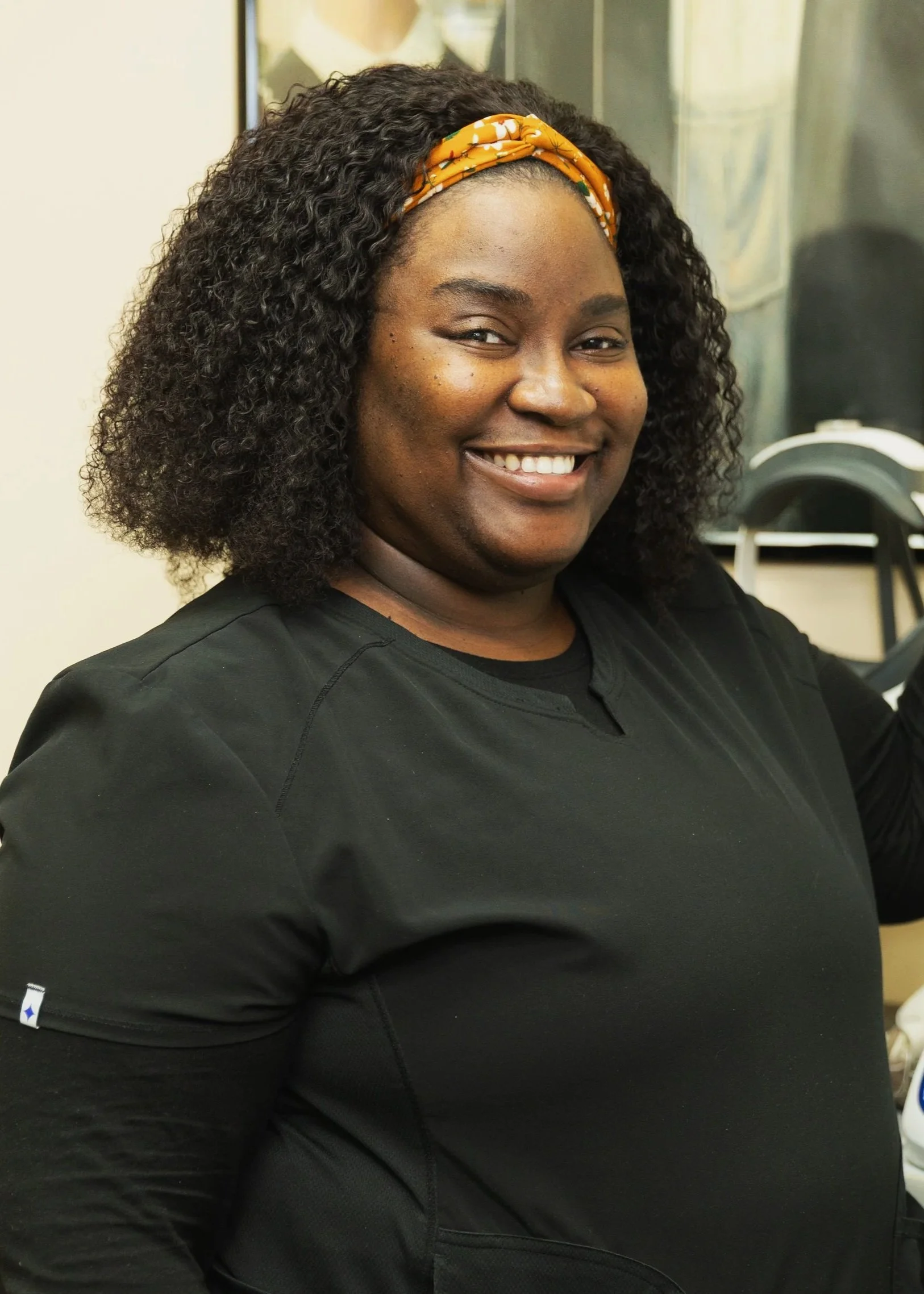A smiling woman with curly black hair wearing a black shirt and an orange headband.