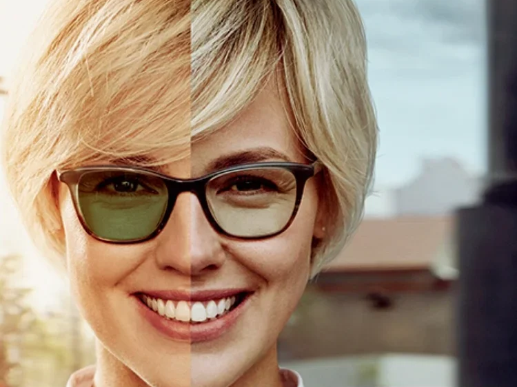 Close-up of a smiling woman with blonde hair, wearing glasses, outdoors with a blurred background.