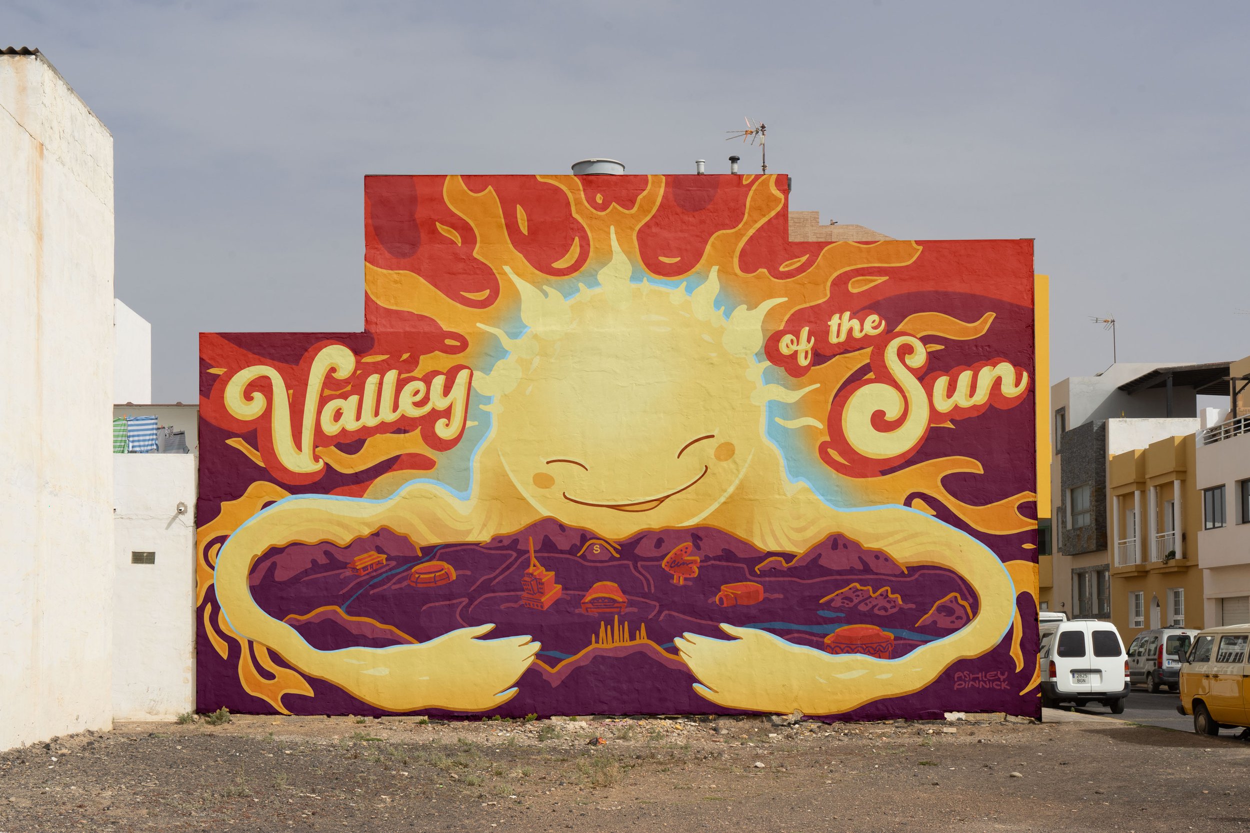 Colorful mural of a smiling sun with outstretched arms, holding a valley with landmarks, titled "Valley of the Sun".