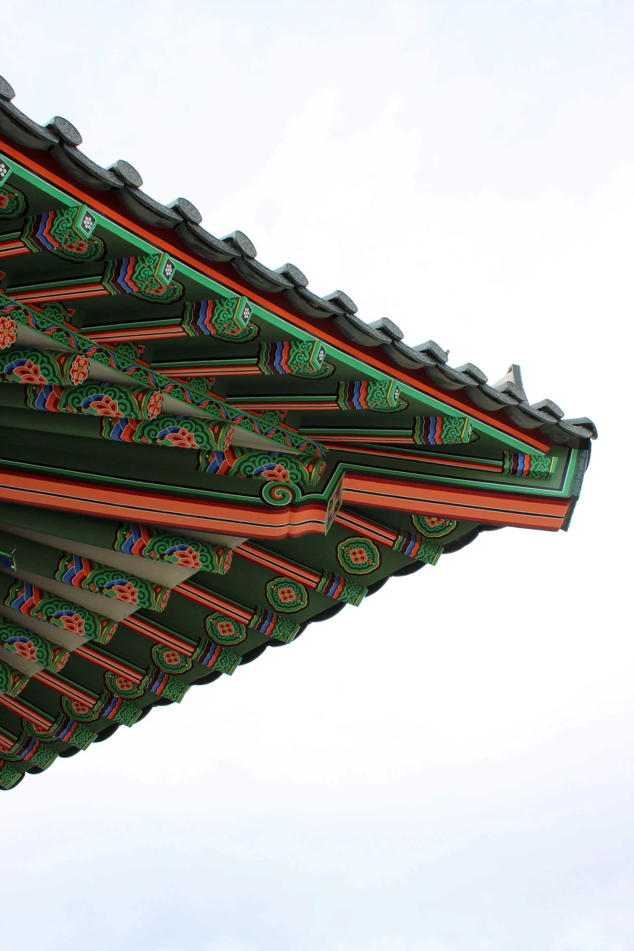 Close-up of a traditional Asian-style roof with colorful ornate patterns, against a light sky background.