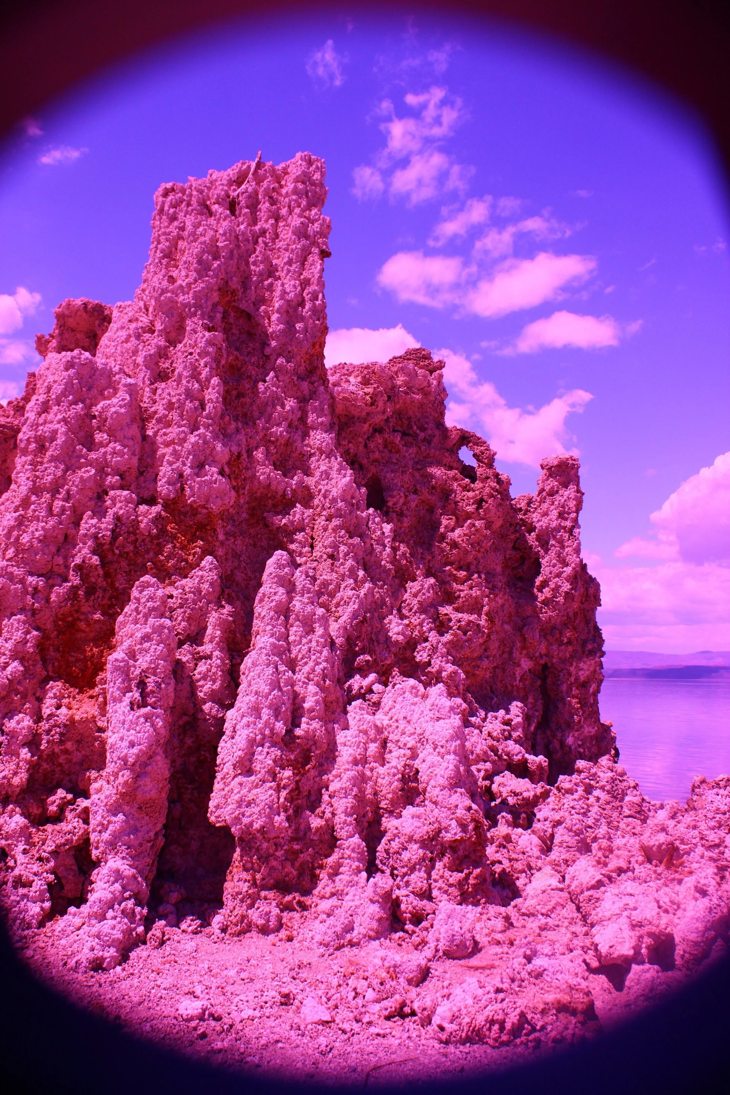 Pink rock formation near a body of water under a blue sky with clouds