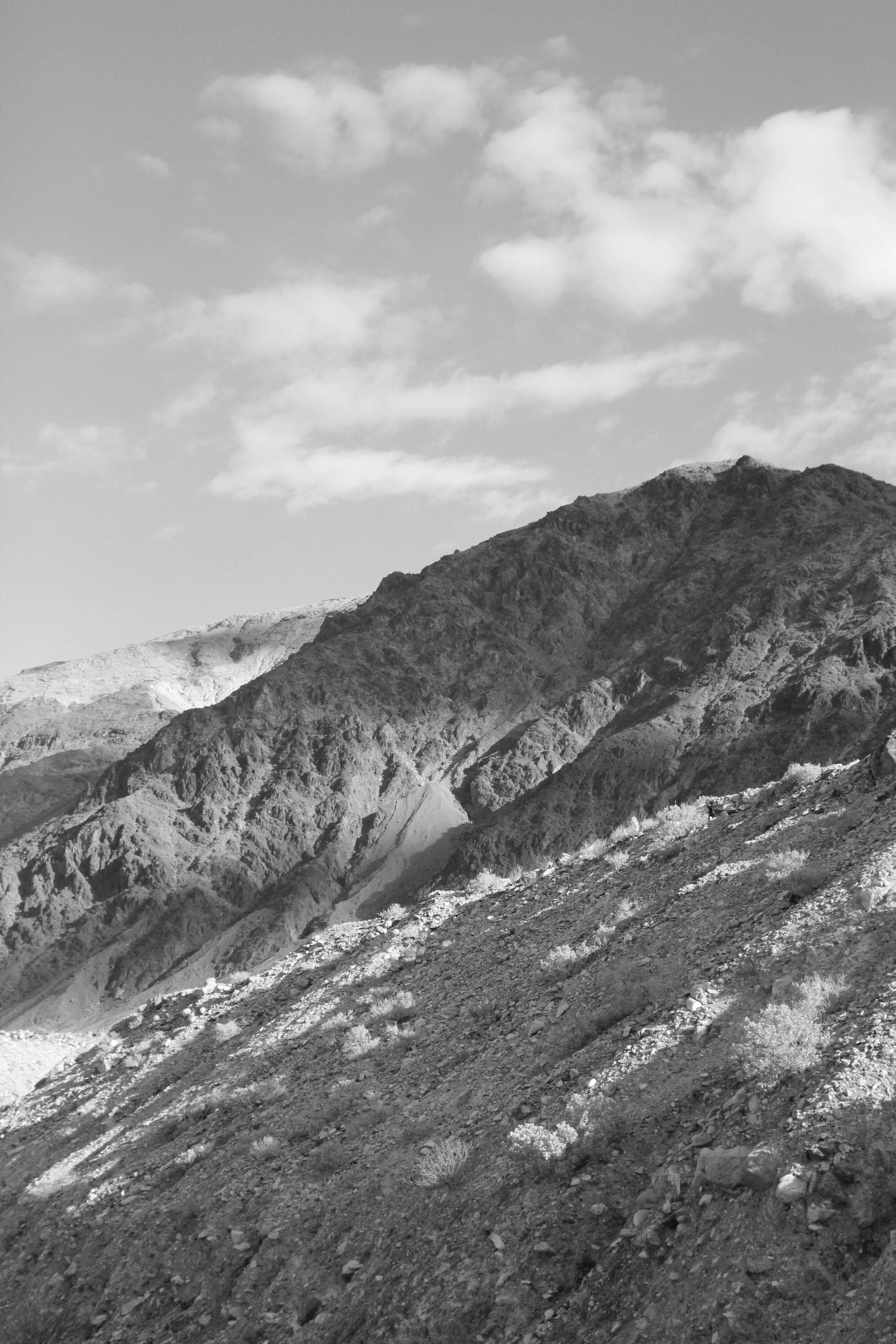 Black and white photo of rocky mountain terrain with sparse vegetation and a partly cloudy sky.