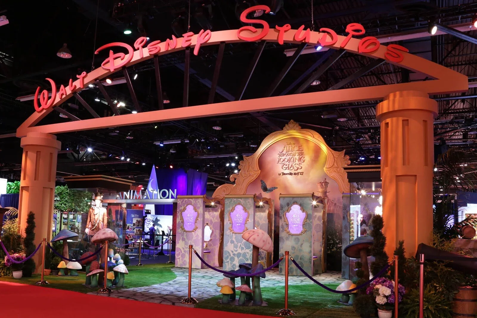 Disney Studios exhibit at an event, featuring an Alice in Wonderland theme with whimsical mushrooms, ornate frames, and a large sign saying "Walt Disney Studios."