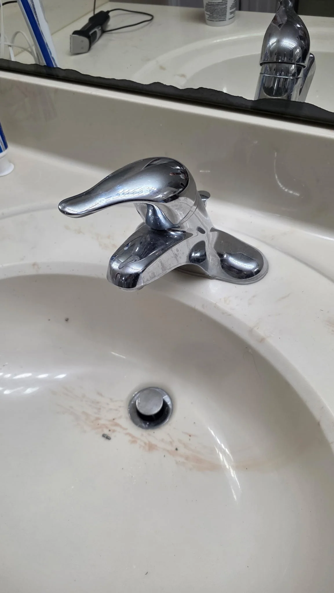 A bathroom sink with a chrome faucet, a mirror above, and some cleaning supplies and a razor visible on the counter.