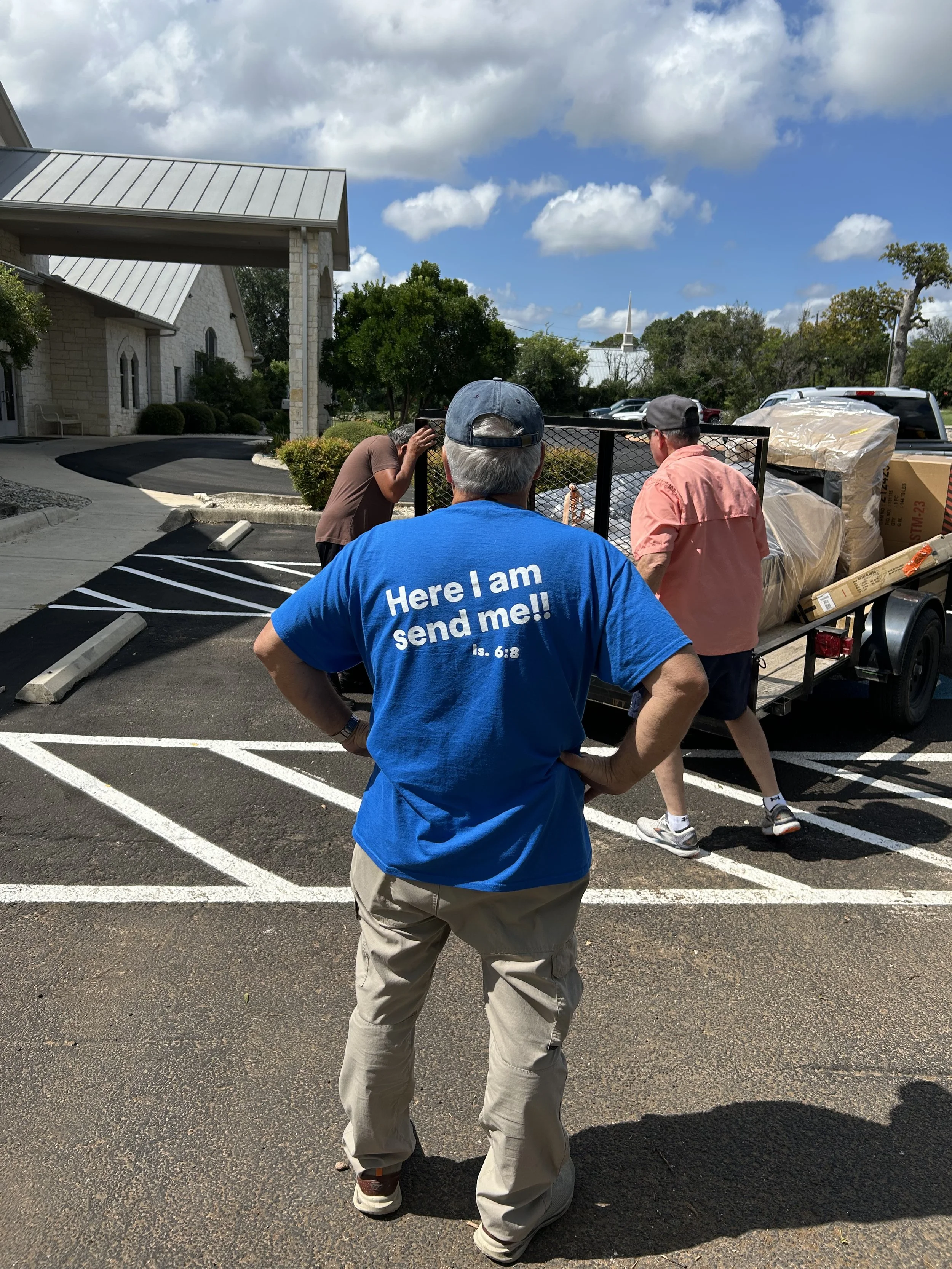 Volunteer helping load a trailer wearing a shirt that reads "Here I am. Send me."