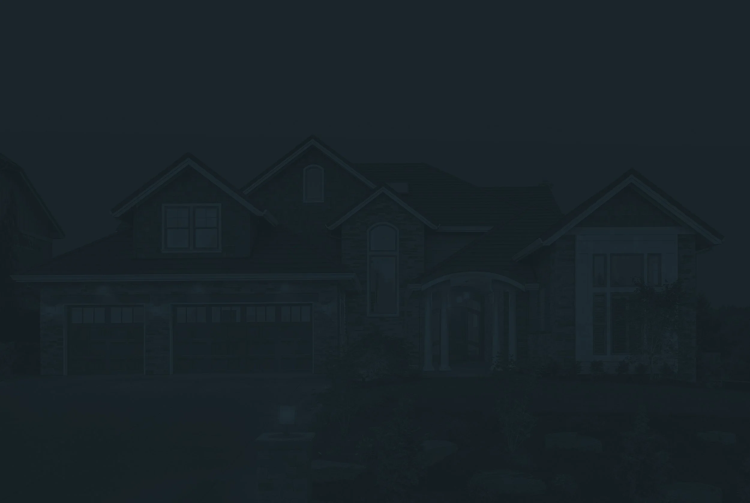 Image of a large, modern house with multiple gables, brick and siding exterior, front porch, and a garage, taken at dusk or night.