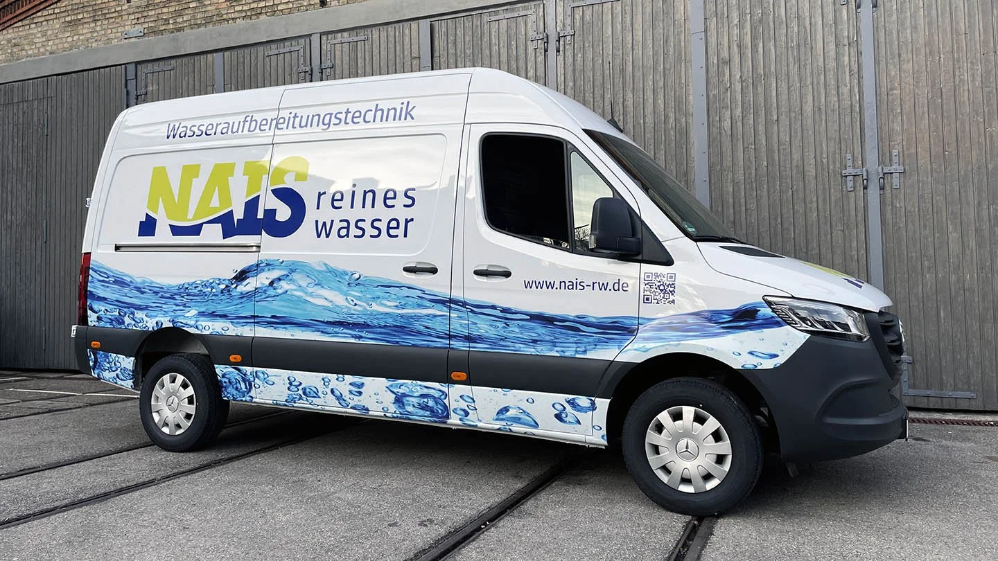 Weißer Lieferwagen mit Wasserlogo und blauer Wasserwelle, Werbung für sauberes Wasser, mit Website und QR-Code, vor einer Holztorwand.