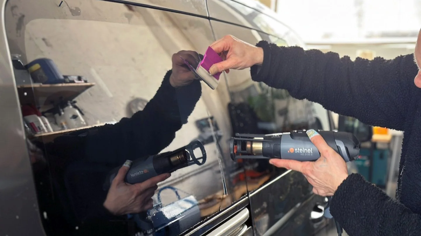 Eine Person reinigt eine Autocarrosserie mit einem Heißluftfön.