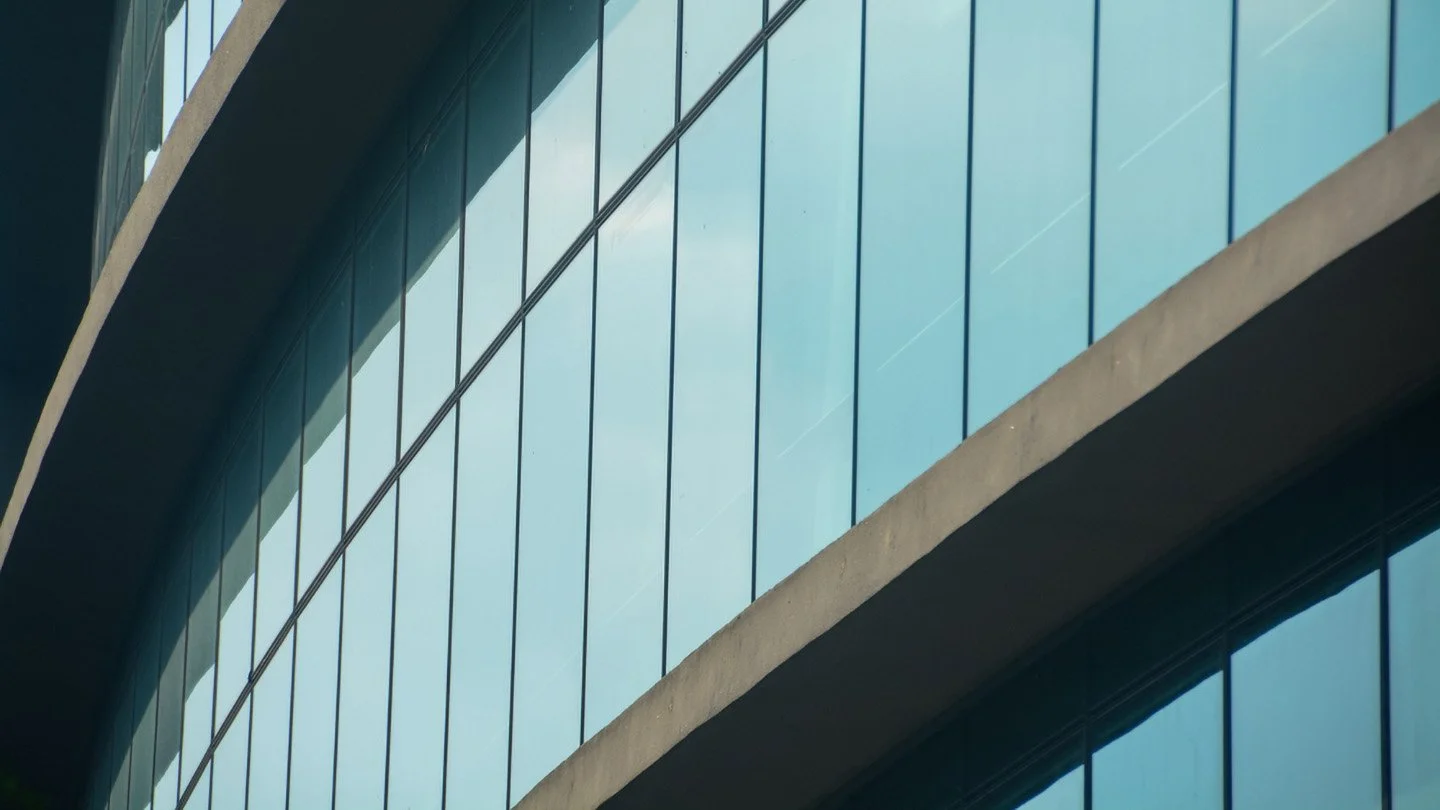 Blick auf die Glasfassade eines modernen Gebäudes mit reflektierendem Himmel und Wolken