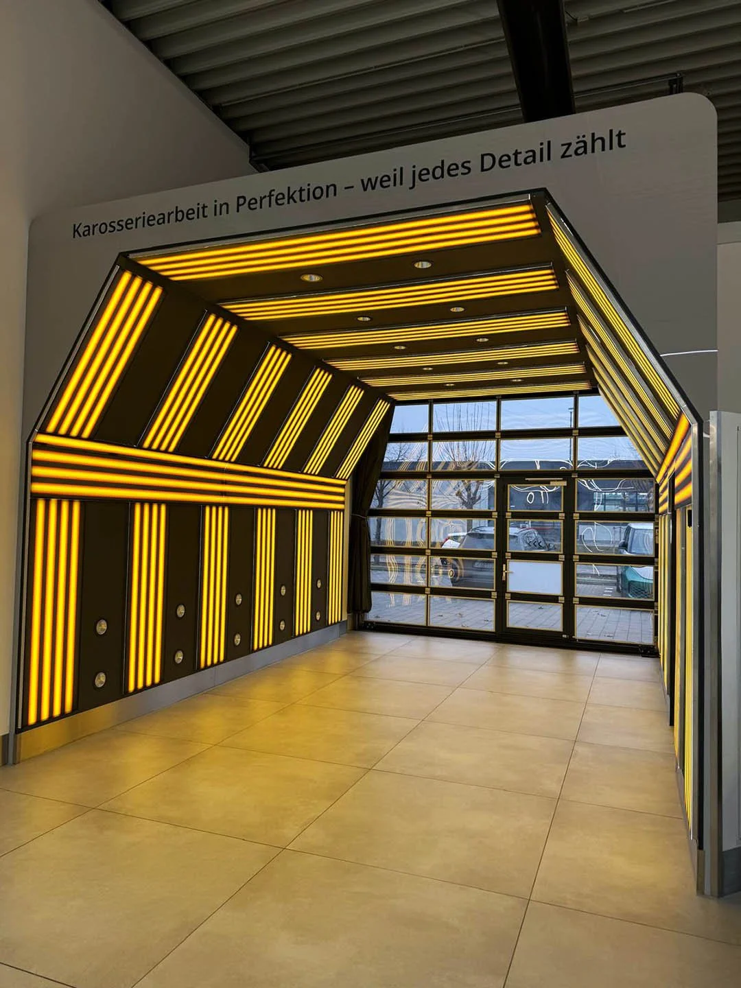 Innenaufnahme mit beleuchteter Wandgestaltung in Schwarz und Gelb, große Fensterfront, heller Boden.