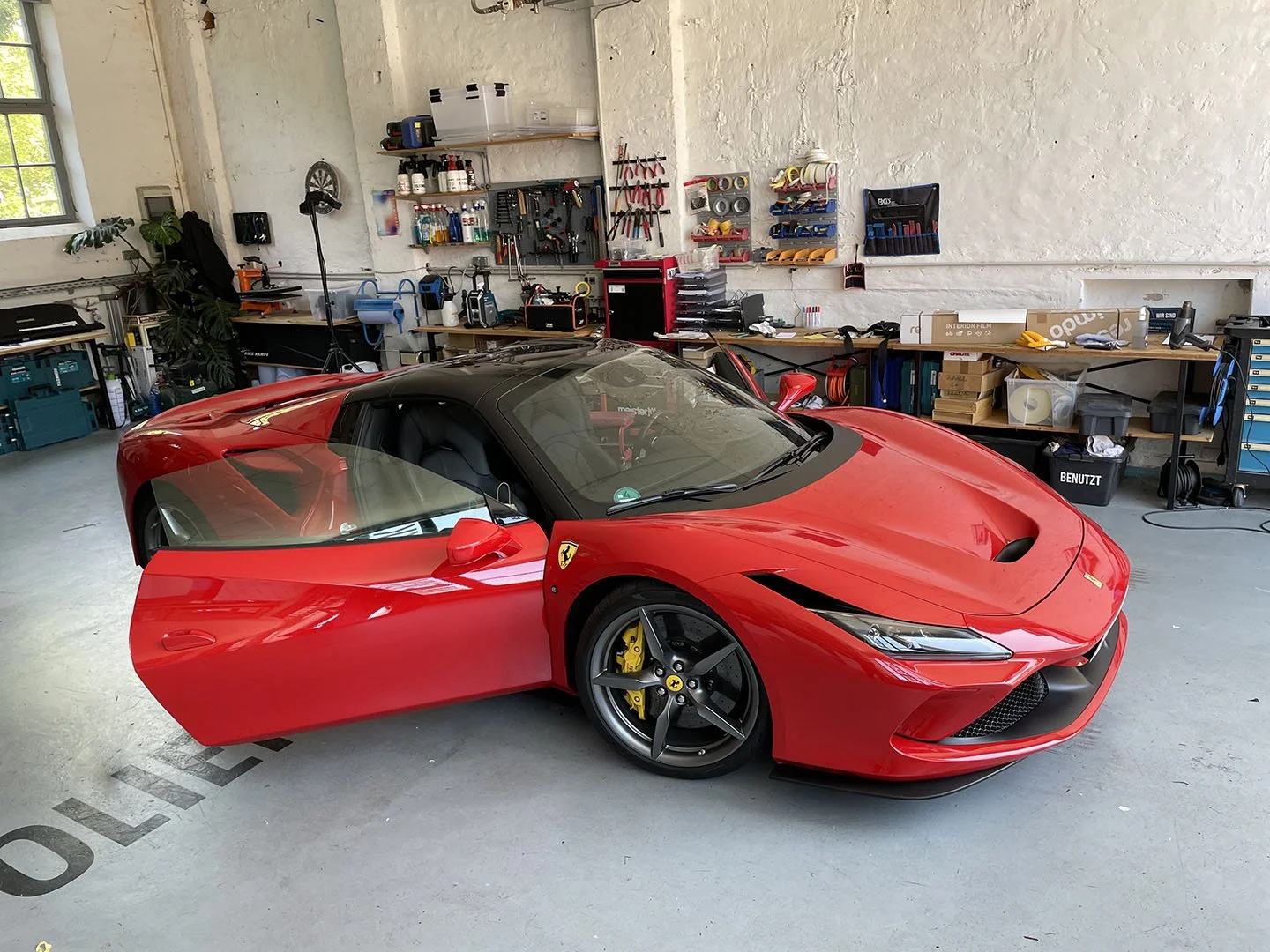 Roter Ferrari-Sportwagen in einer Werkstatt, umgeben von Werkzeugen und Werkbänken.