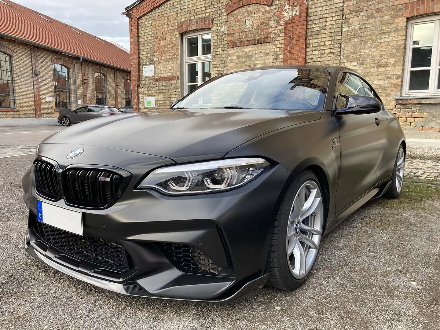 Ein schwarzer BMW M2 mit sportlichem Design, vor historischem Backsteinhaus geparkt.