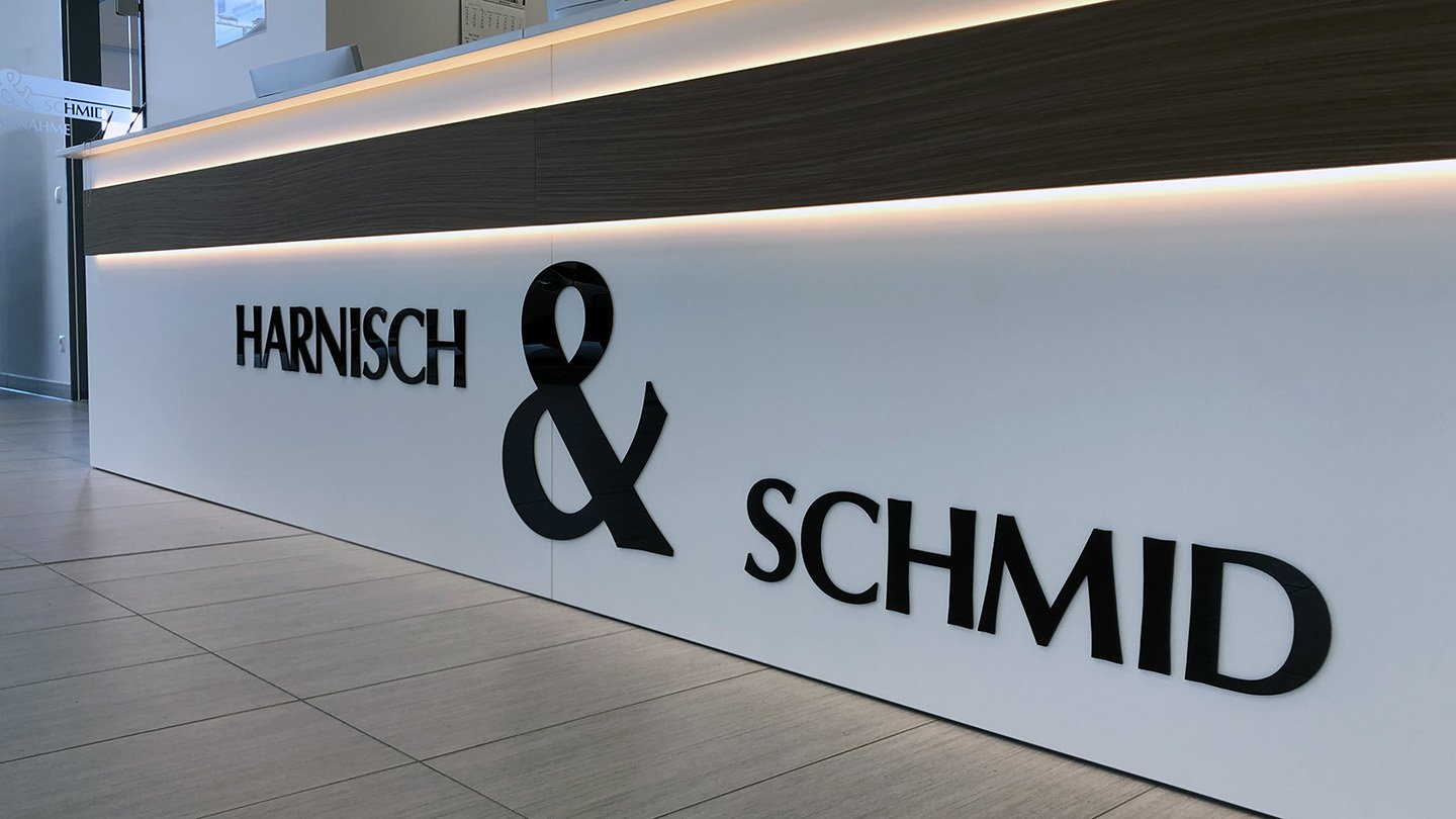 Innenaufnahme eines Empfangstresens mit 3D-Acrylbuchstaben in schwarzer Schrift auf weißer Oberfläche.