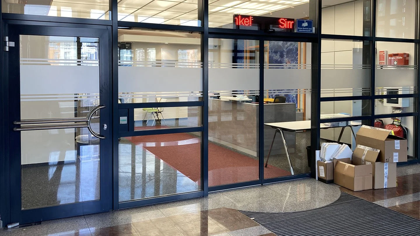 Eingangsbereich eines Büros mit Glasschiebtüren, Kartons und einem Empfangstresen