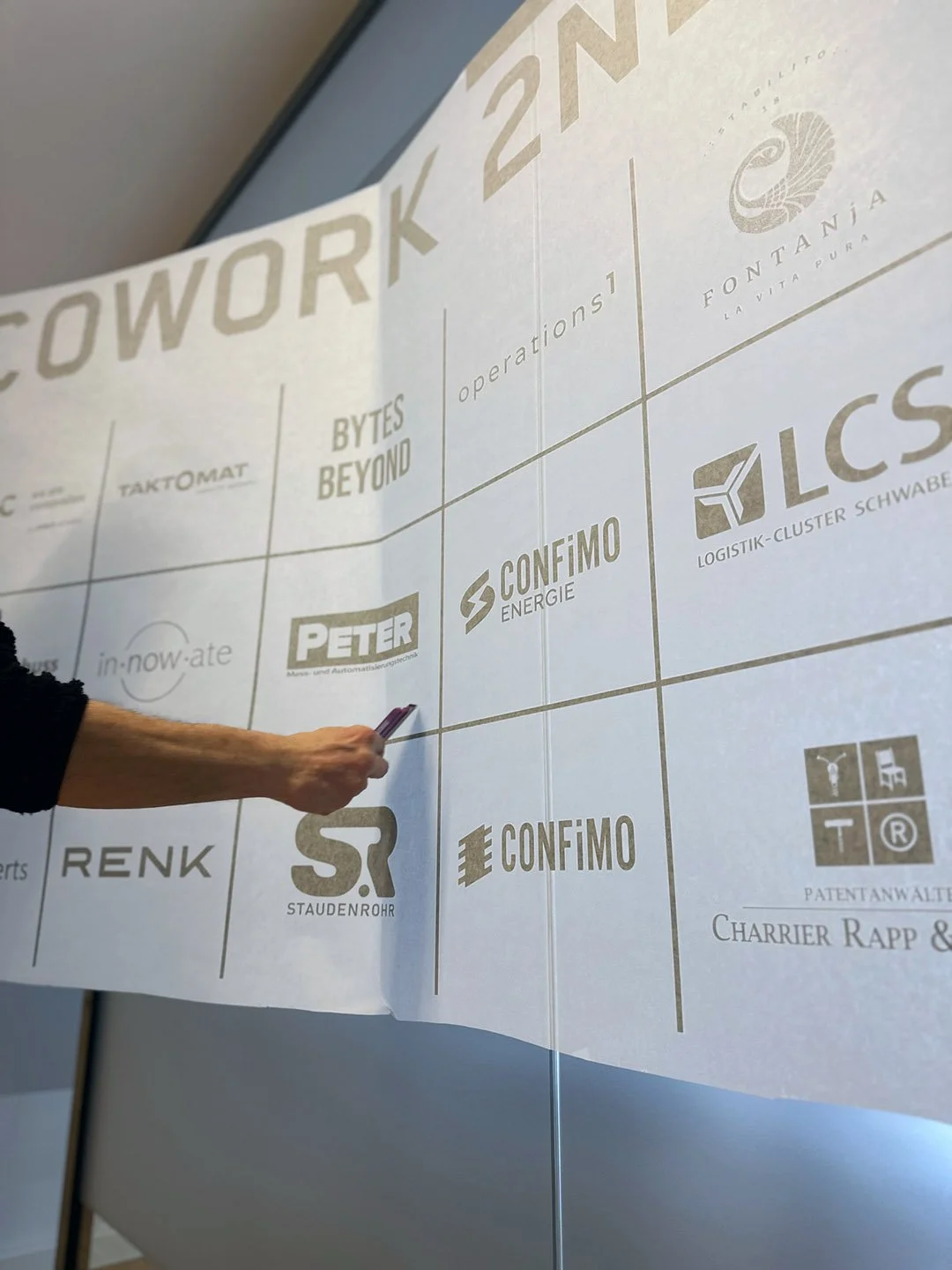 Ein Blick auf eine große whiteboard-ähnliche Tafel mit Firmenlogos und Texten, die sich auf den Bereich Logistik, Energie und Automatisierung beziehen, mit einer Hand, die einen Stift hält und Notizen macht.