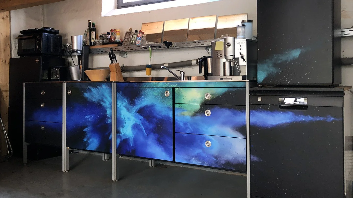 Küchenschränke mit Weltraum-Motiv, Küchenutensilien, Kaffeemaschine, Mikrowelle und Kühlschrank in einer Küche.