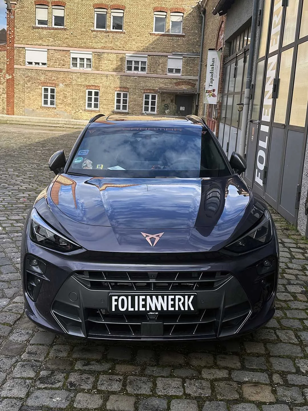 Schwarzer Sportwagen auf gepflasterter Straße vor historischen Ziegelgebäuden.