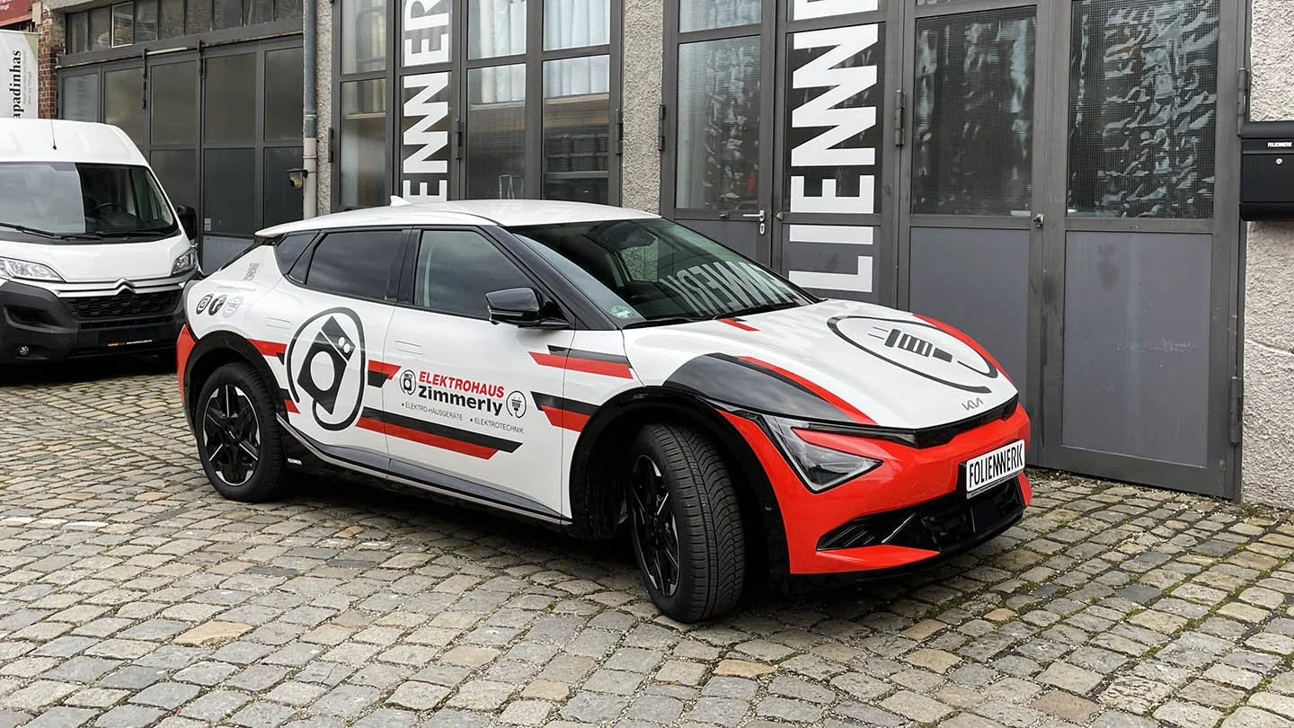 Ein weißes Auto mit rotem und schwarzem Design, Parken vor einem Gebäude mit grauen Türen, und einem weißen Van im Hintergrund.