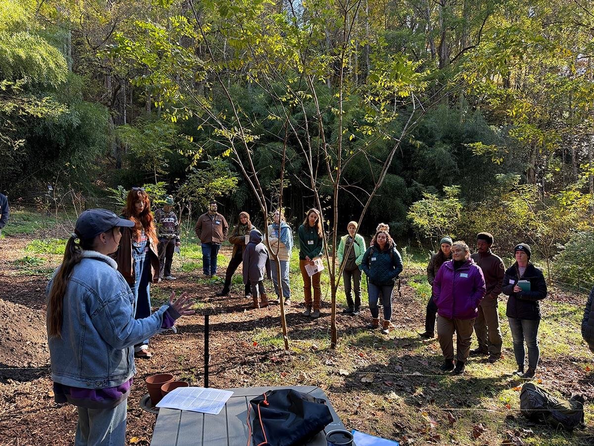 speaker-sydney-kale-speaking-to-a-group-of-people-in-a-clearing-with-planted-trees.jpg