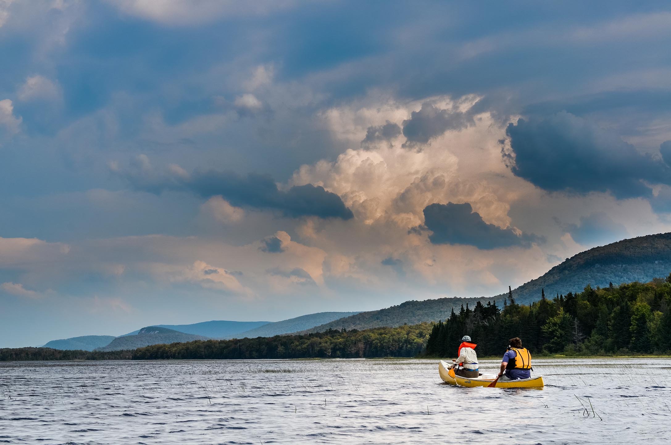 two-people-in-yellow-canoe-paddling-on-lake-in-the-champlain-adirondack-biosphere-network.jpg