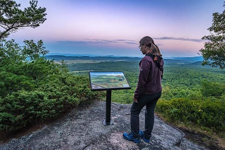 Woman reading interp sign at Adirondack mountain overlook spot in the Champlain-Adirondack Biosphere Network.