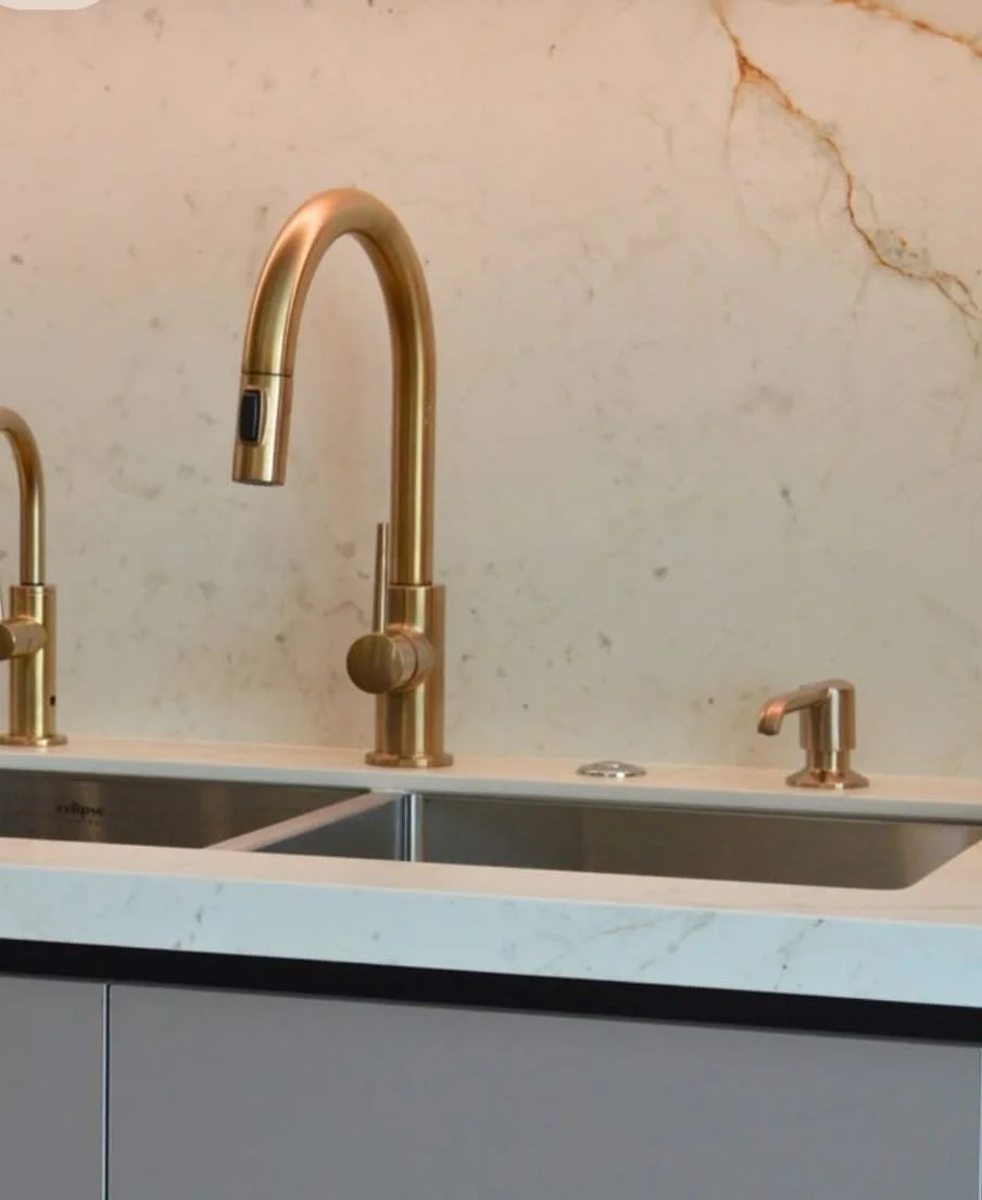 Grifo de oro junto a un fregadero en una cocina moderna con encimera de mármol.